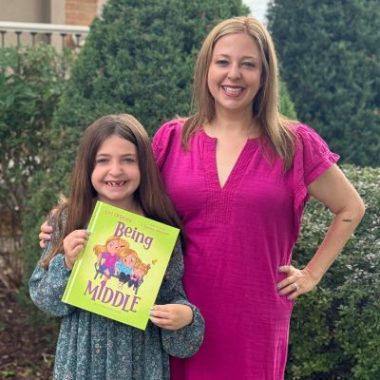 Author Lori Orlinsky, blond hair, standing next to her middle daughter, a brunette holding her book Being Middle, both smiling at the camera.