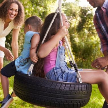 Parents pushing children on tire swing during family playtime