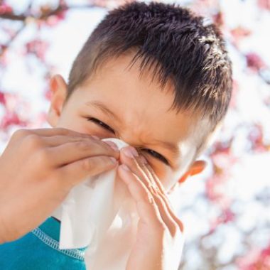 Child with seasonal allergies rubbing itchy eyes and nose outdoors during spring allergy season